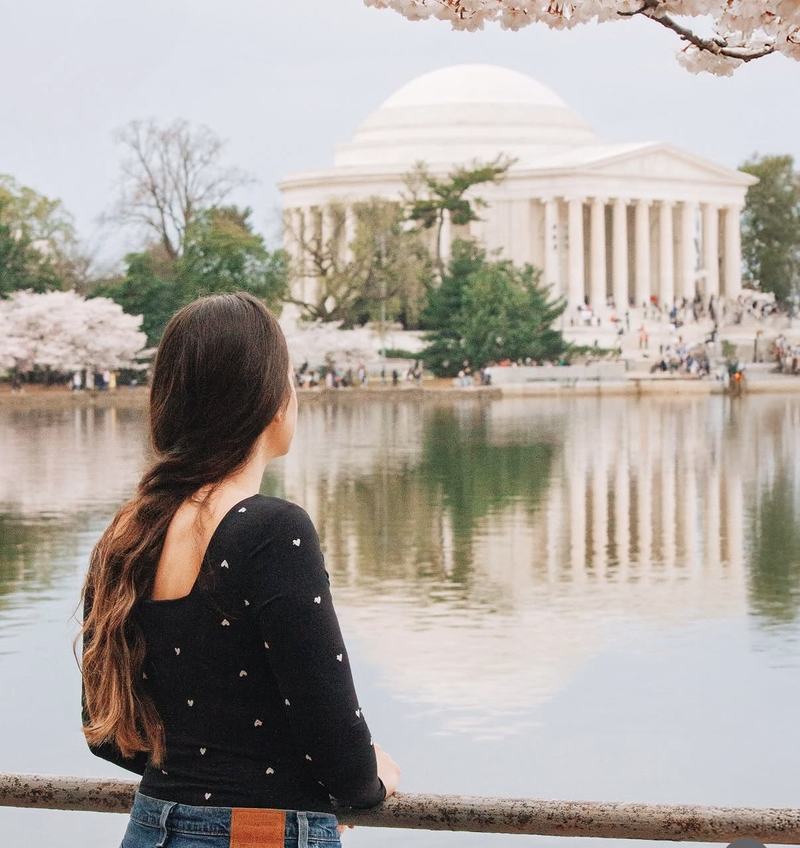 Woman under cherry blossoms looking across the water at the Jefferson Memorial